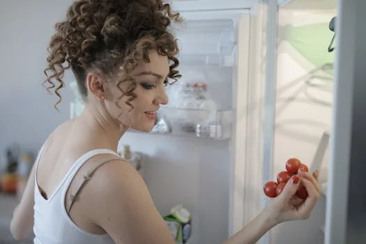 A woman holding tomatoes in front of an open refrigerator.